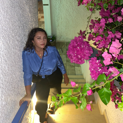 photo de Klara avec une chemise bleue, un panatalon noir, des marches et des fleurs roses